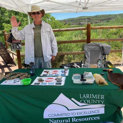 Volunteer standing behind table set up at trailhead with educational activities.